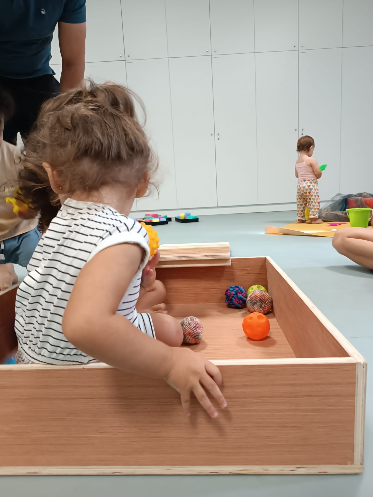 Un tout-petit debout explore une caisse en bois remplie de balles colorées