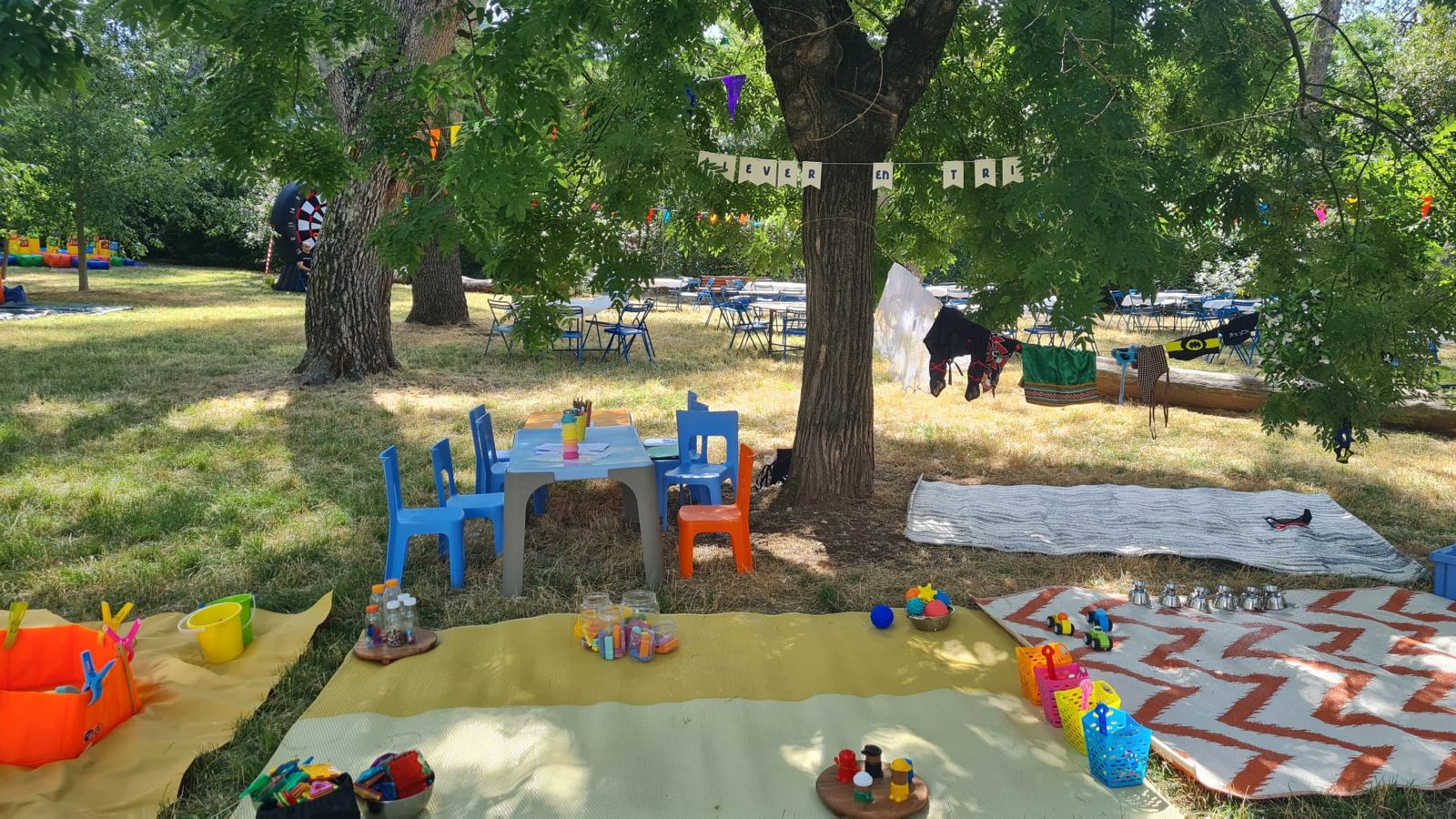 Espace de jeu installé en extérieur sous les arbres : tapis, petite table et chaises pour les enfants